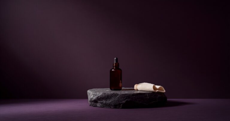 Frasco de vidrio ámbar con cuentagotas sobre piedra oscura, junto a un paño de lino, entre sombras ciruela.