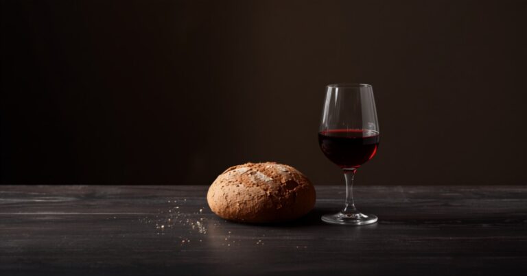 Hogaza de pan rústico y copa de vino tinto sobre madera oscura en penumbra.