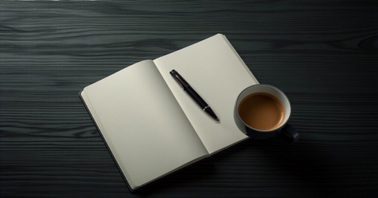Bodegón en penumbra con una pluma estilográfica sobre un cuaderno abierto en blanco junto a una taza de café sobre madera oscura.